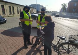 Na zdjęciu widoczni są policjanci ruchu drogowego w trakcie rozmowy i wręczania gadżetów profilaktycznych rowerzystce.