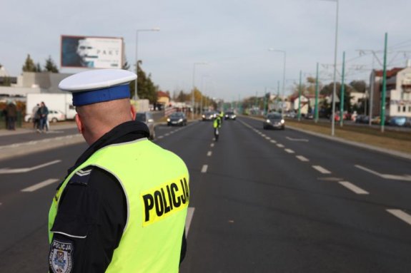 Zdjęcie przedstawia policjanta ruchu drogowego stojącego tyłem do obiektywu.