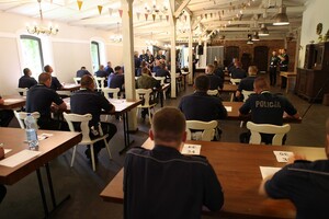 Zdjęcie przedstawia funkcjonariuszy ruchu drogowego siedzących przy stolikach w oczekiwaniu na przystąpienie do testu wiedzy.