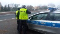 Zdjęcie przedstawia policjantów ruchu drogowego stojących przy oznakowanym radiowozie.