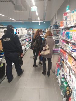 Na zdjęciu widać umundurowanego policjanta i dwie kobiety między regałami sklepowymi.
