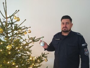 Zdjęcie przedstawia umundurowanego policjanta trzymającego bombkę wiszącą na choince.