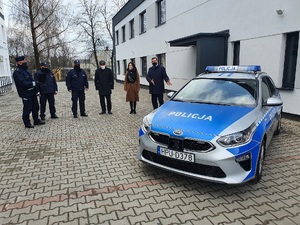 Na zdjęciu widoczny jest oznakowany radiowóz oraz kilka osób stojących w pobliżu.