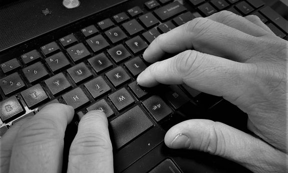 Na zdjęciu widoczna jest klawiatura komputerowa i ludzkie dłonie na niej.
