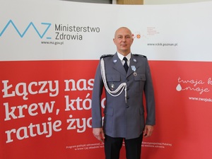 Zdjęcie przedstawia policjanta stojącego w umundurowaniu wyjściowym.