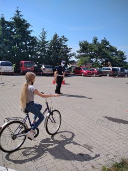Na zdjęciu widać dziecko na rowerze a na dalszym planie policjanta ruchu drogowego.