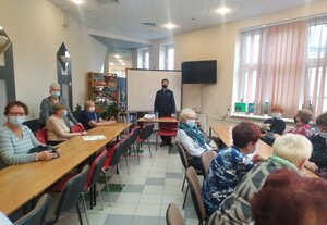 wzdłuż ciągu stolików, zasiadają seniorzy, w głębi widoczna umundurowana policjantka