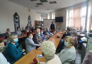 wzdłuż ciągu stolików, zasiadają seniorzy, w głębi widoczna umundurowana policjantka